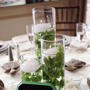 the table is set with candles, flowers and greenery in glass vases on it