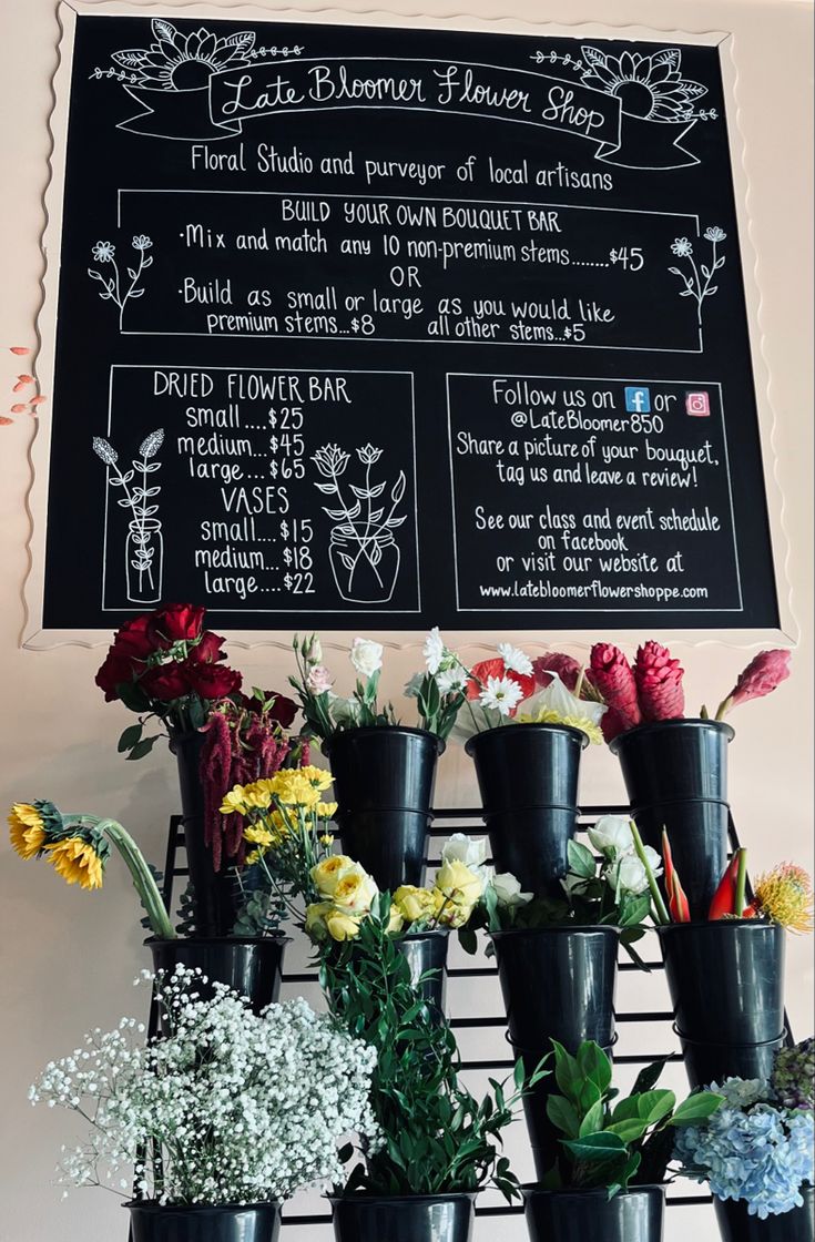 flowers are arranged in black vases next to a chalkboard