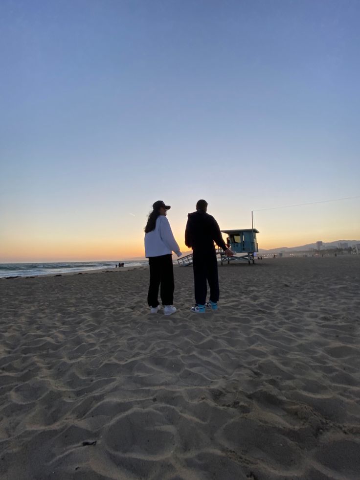 two people are standing on the beach at sunset