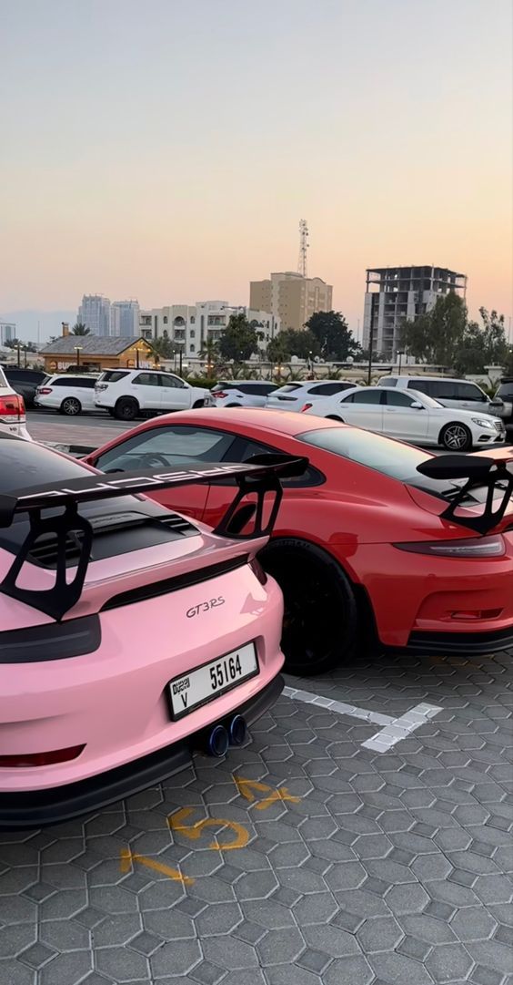 two pink sports cars parked next to each other in a parking lot