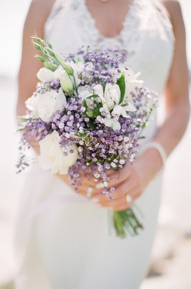 a bride holding a bouquet of white and purple flowers on her wedding day at the beach