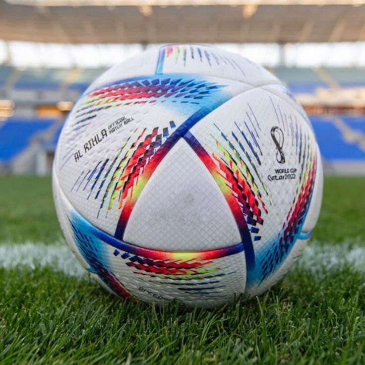 a soccer ball sitting on top of a lush green field in front of a stadium