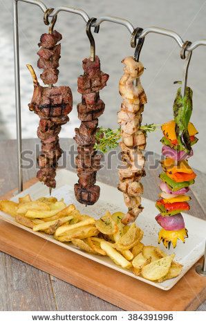 several skewered meats and french fries on a tray