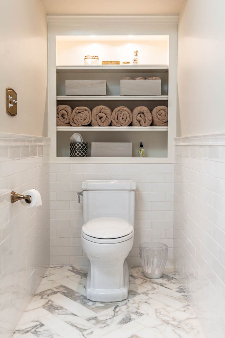 a white toilet sitting inside of a bathroom next to a shelf filled with lots of towels