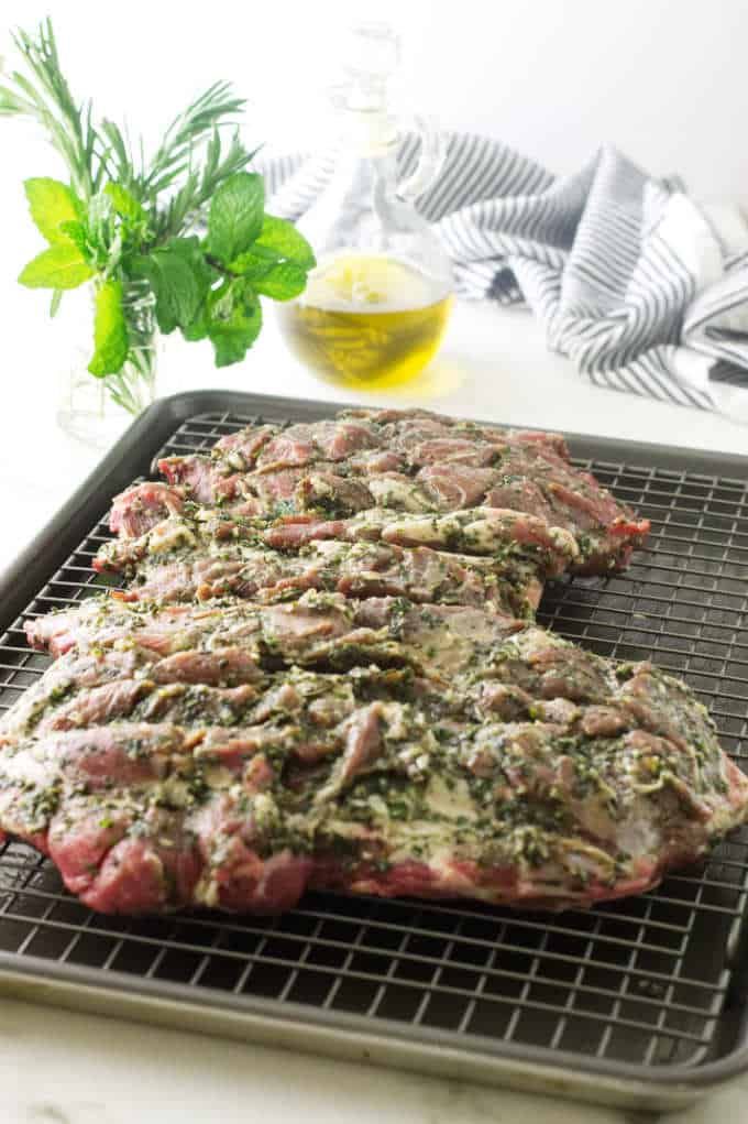 two steaks on a grill with herbs and seasoning next to it, sitting on a cooling rack