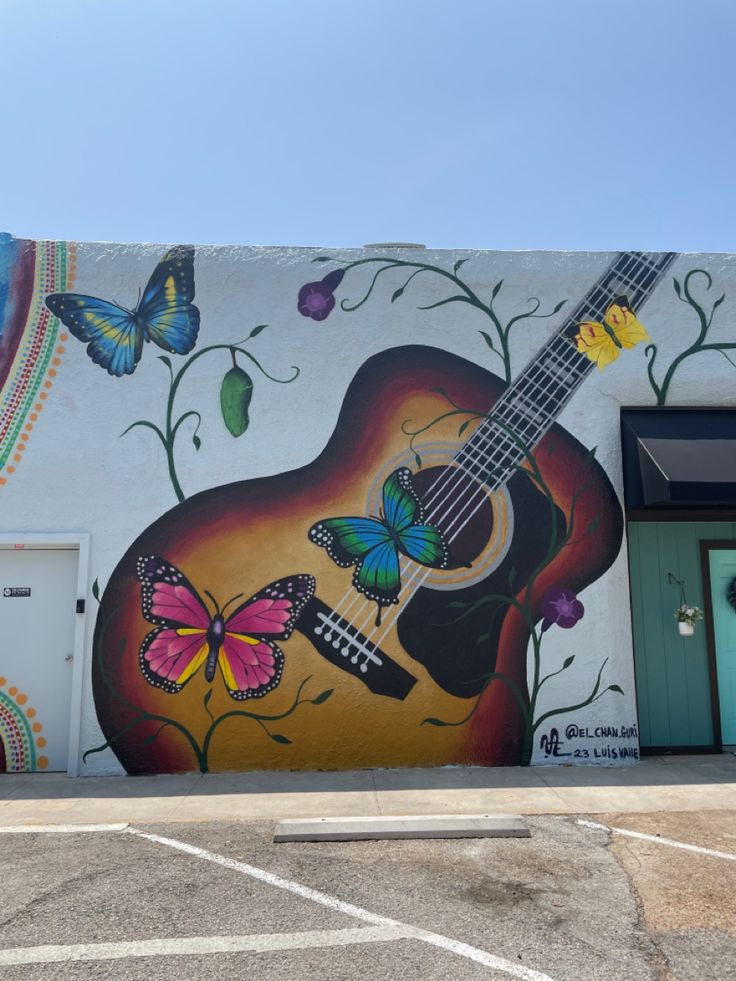 a painting of a guitar and butterflies on the side of a building in front of a garage