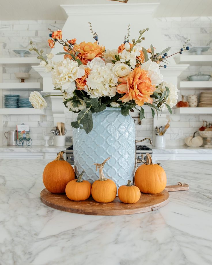 a blue vase filled with white and orange flowers on top of a counter next to pumpkins