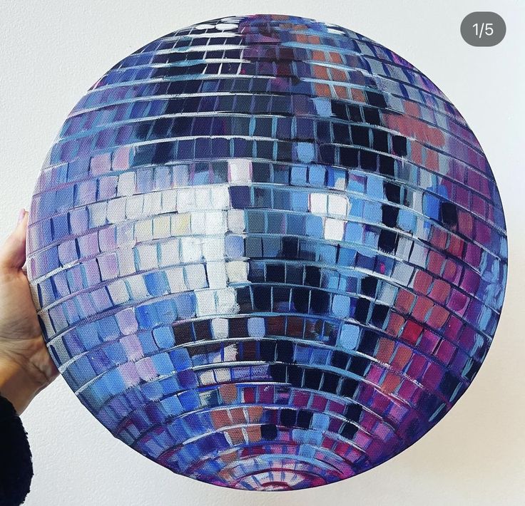 a person holding up a disco ball with the reflection of them in it's center