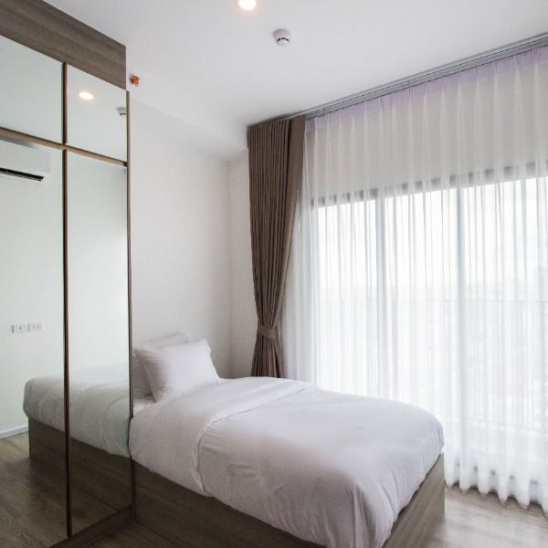 a white bed sitting next to a large window in a room with wooden flooring