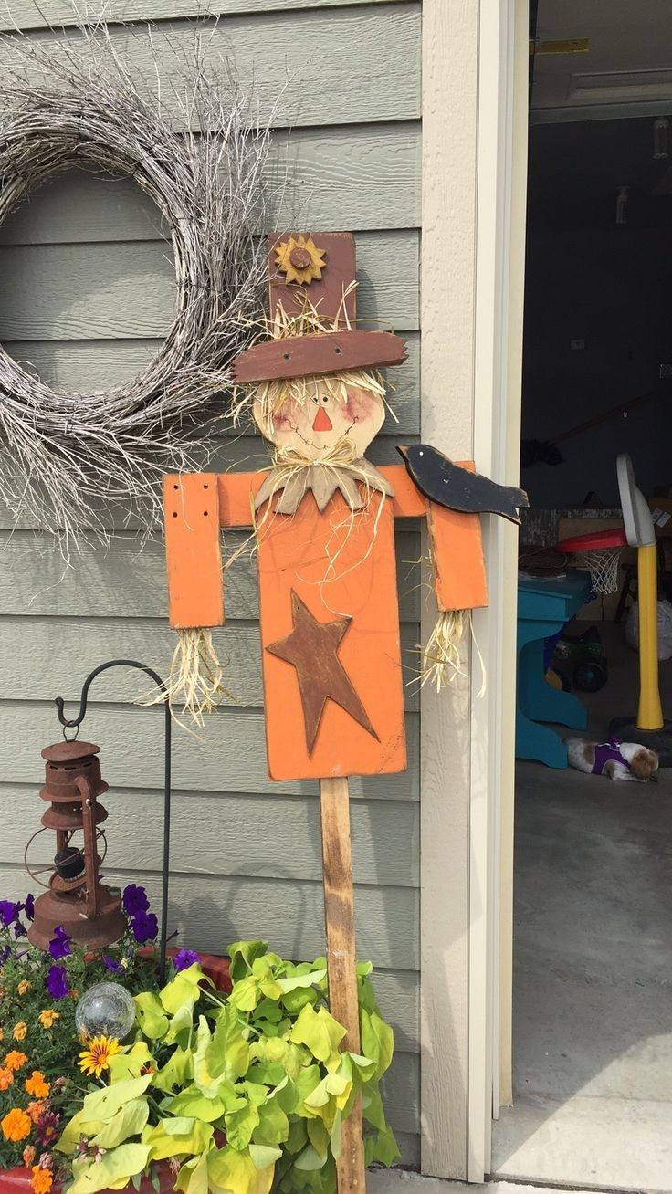 a scarecrow is hanging on the side of a house next to a wreath and some flowers