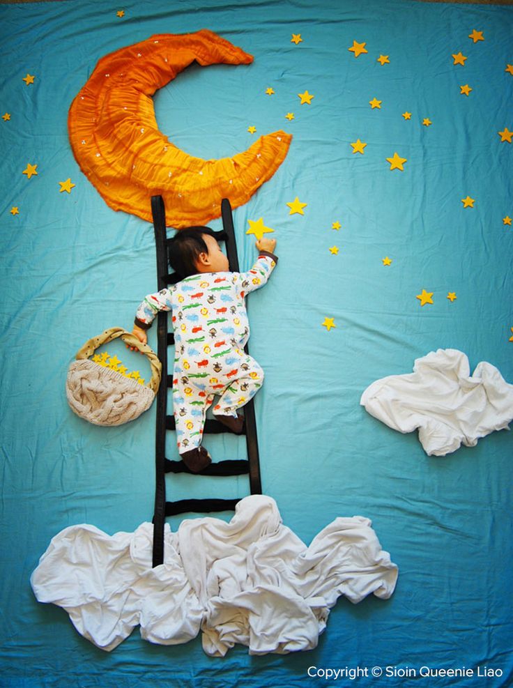 a baby laying on top of a ladder next to an orange moon and star decoration