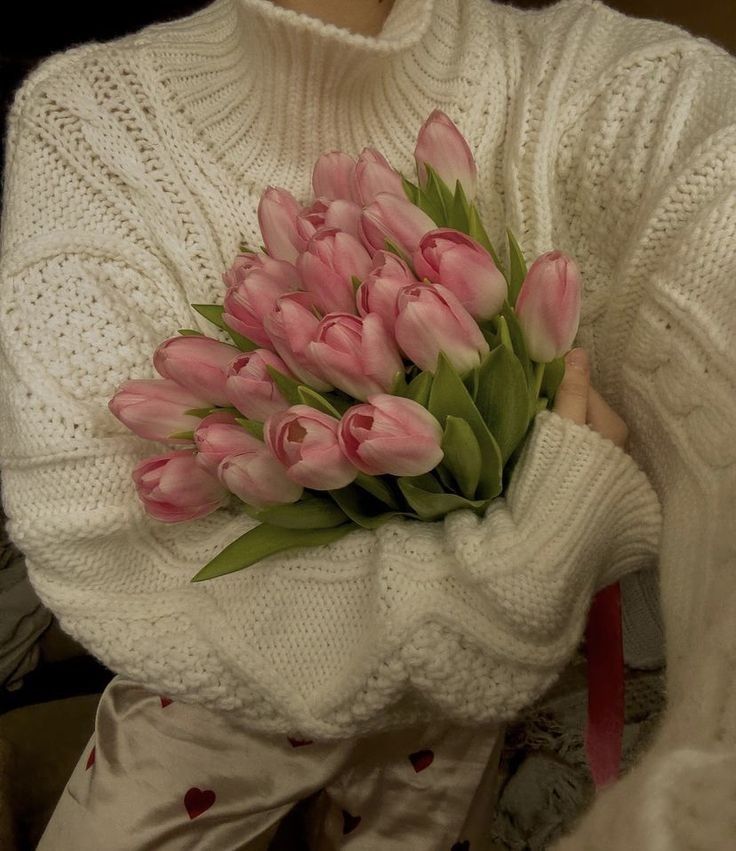 a woman holding a bouquet of pink tulips in her hands while sitting down