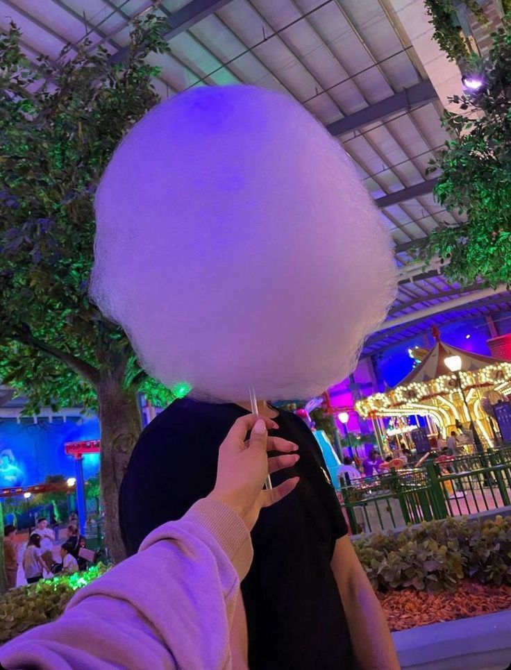 a person holding a giant cotton candy ball in front of their face at an amusement park