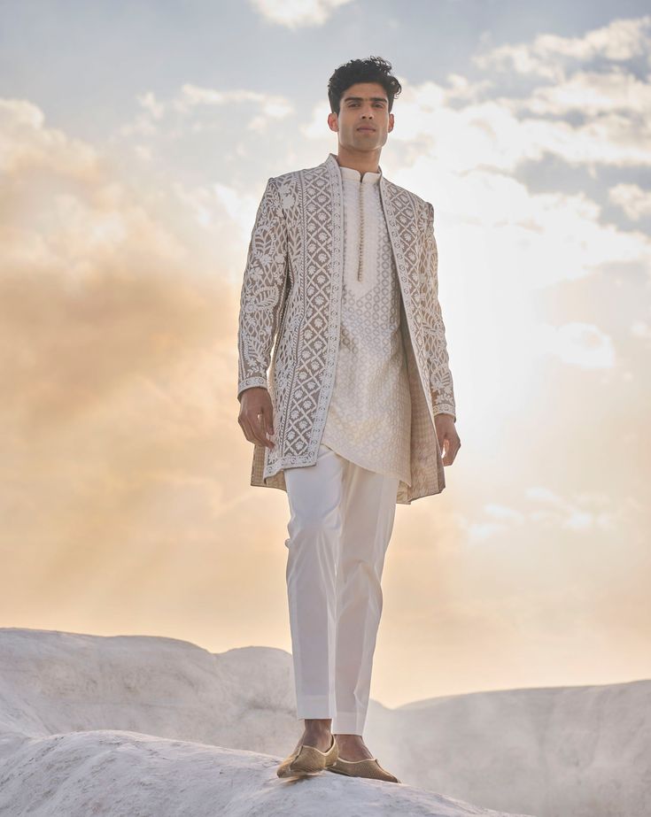 a man standing on top of a snow covered hill wearing a white suit and tie