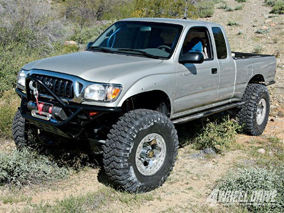 a silver pick up truck parked on top of a grass covered hill in the desert