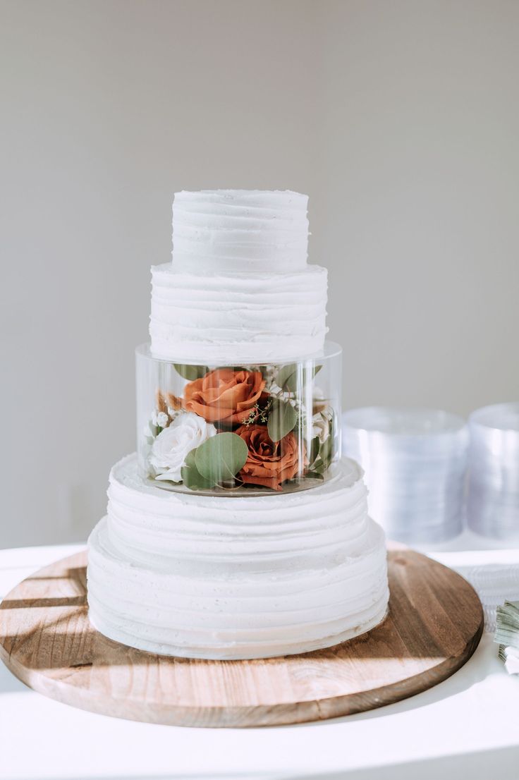 a three tiered cake with flowers in it on a wooden platter next to plates and utensils