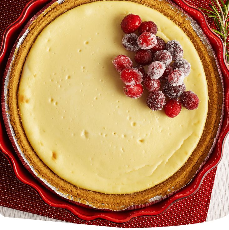 a cheesecake with berries on top is sitting on a red plate next to a sprig of rosemary