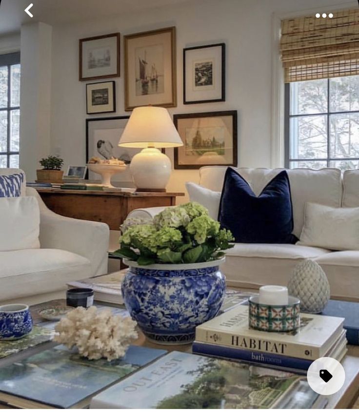 a living room filled with white furniture and blue and white accessories on top of a coffee table