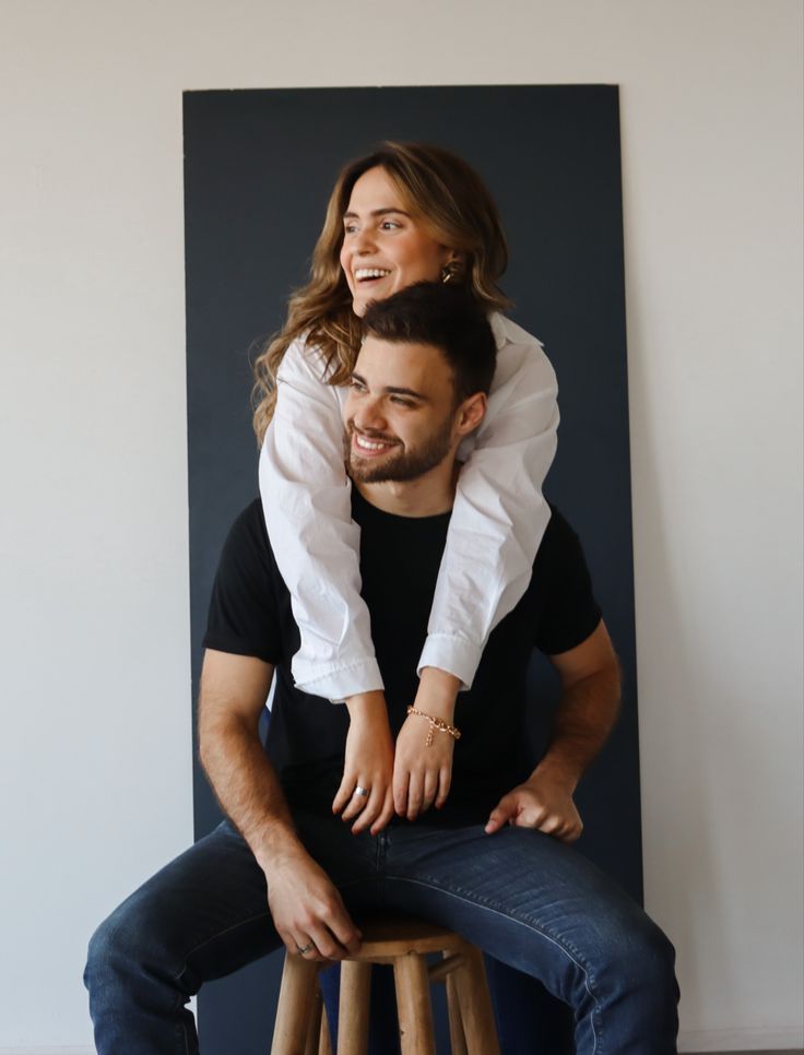 a man sitting on top of a wooden stool next to a woman who is holding her