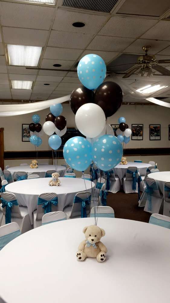 a teddy bear sitting on top of a table with blue and white balloons in the air