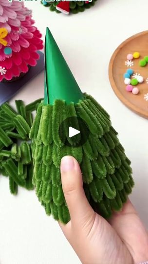 a hand holding a green toy with candy in it's mouth and a flower pot behind it