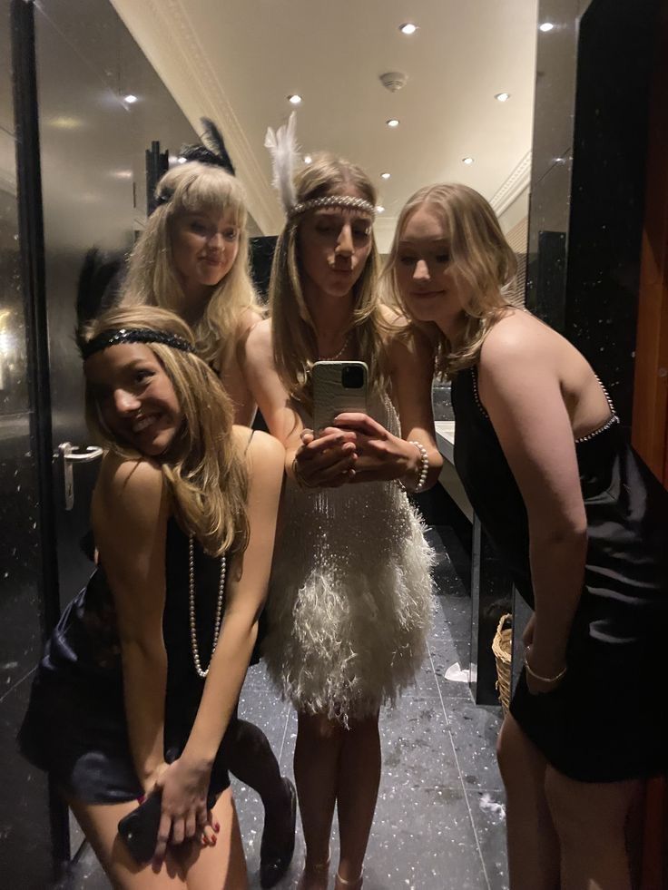 four women taking a selfie in front of a mirror with one woman wearing a feathered dress