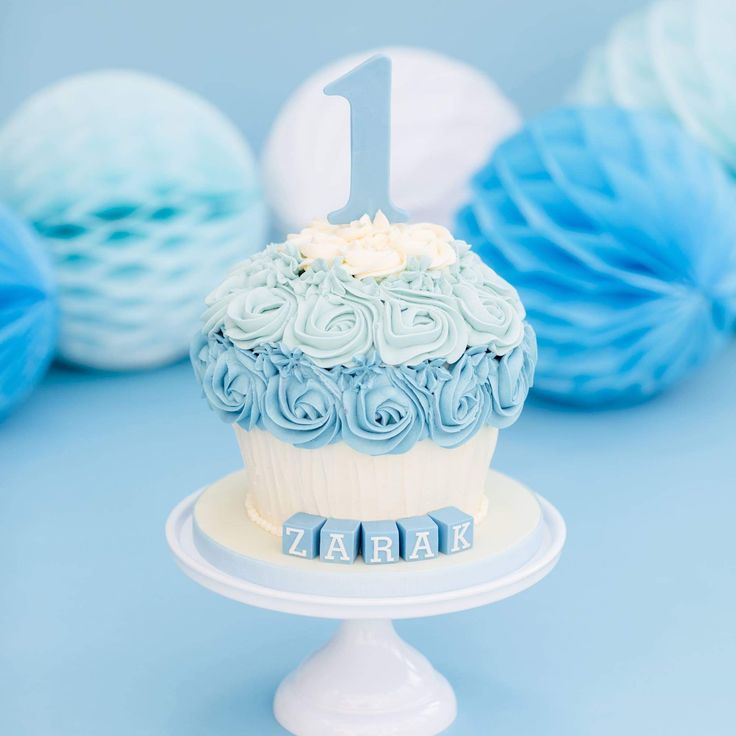 a blue and white cupcake with the number one on it sitting on a cake plate