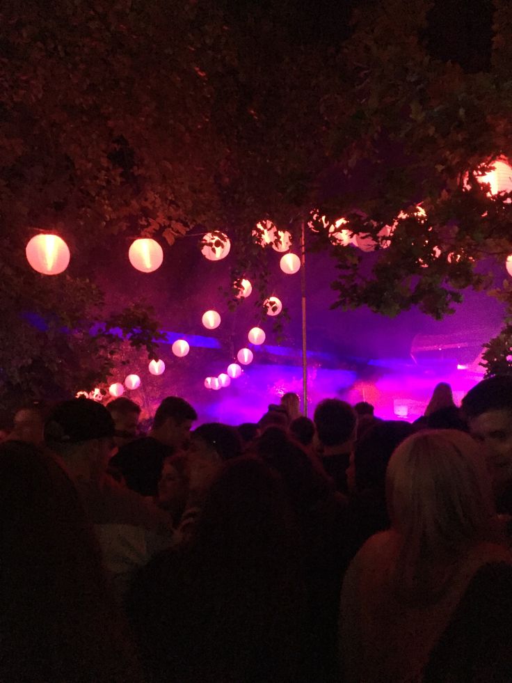 a large group of people standing in front of a purple lit area with paper lanterns hanging from the ceiling