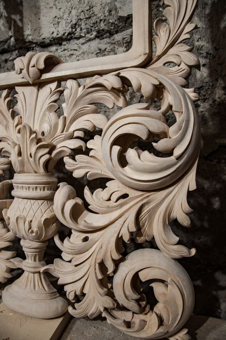 an intricately carved wooden frame with flowers and leaves on the outside, in front of a stone wall