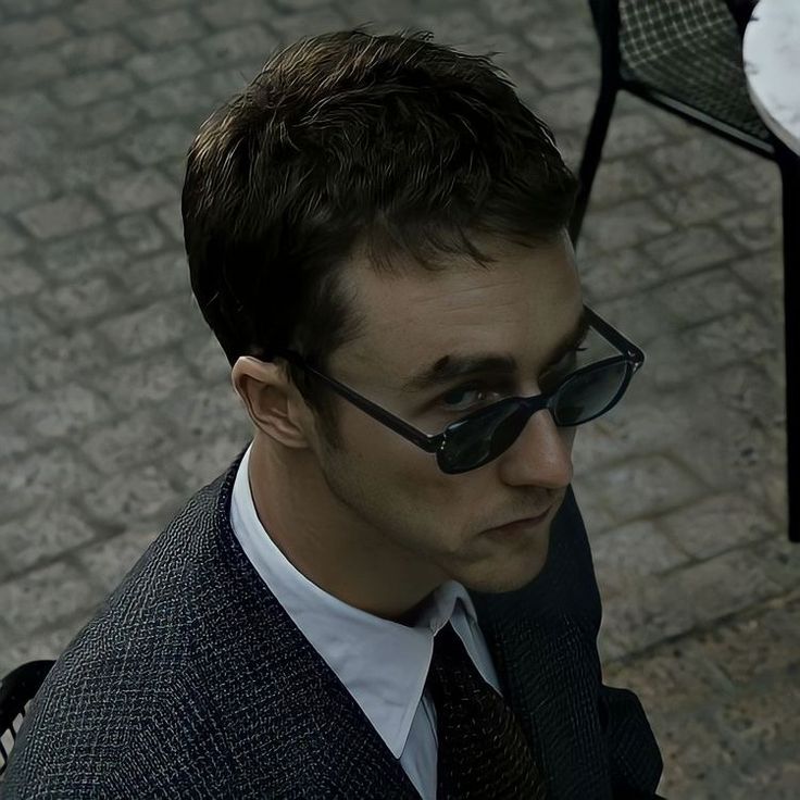 a man wearing sunglasses and a suit looks down at something on the ground in front of him