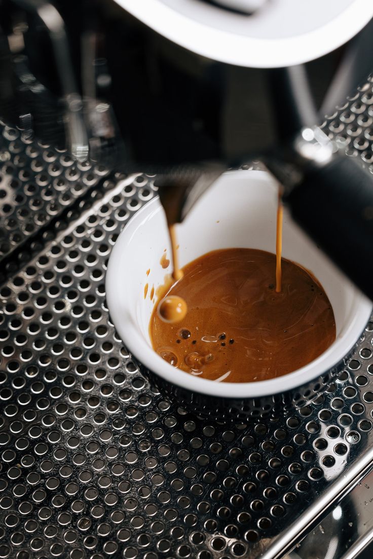 espresso being poured into a white bowl on top of a coffee maker's machine