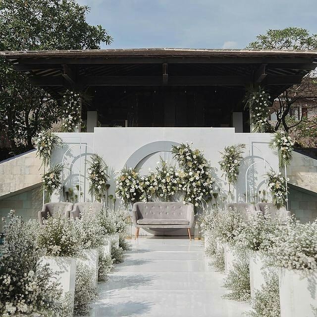 an outdoor wedding venue with white flowers and greenery on the walls, seating for guests