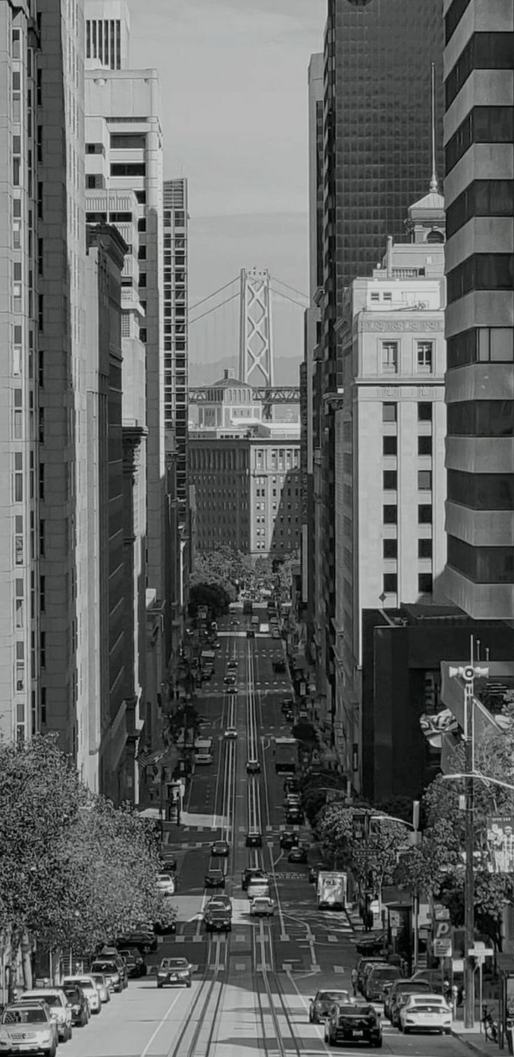 a black and white photo of a city street with cars on the road in front of tall buildings