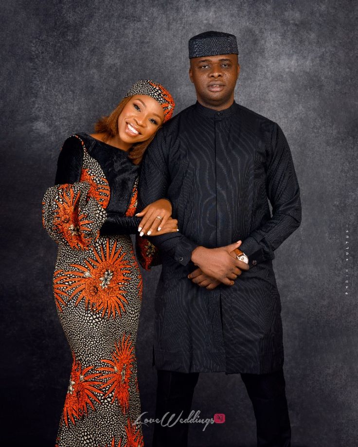 a man and woman standing next to each other in front of a black background with orange flowers