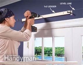 a woman is painting the wall with paint rollers in her living room, and she's measuring the length