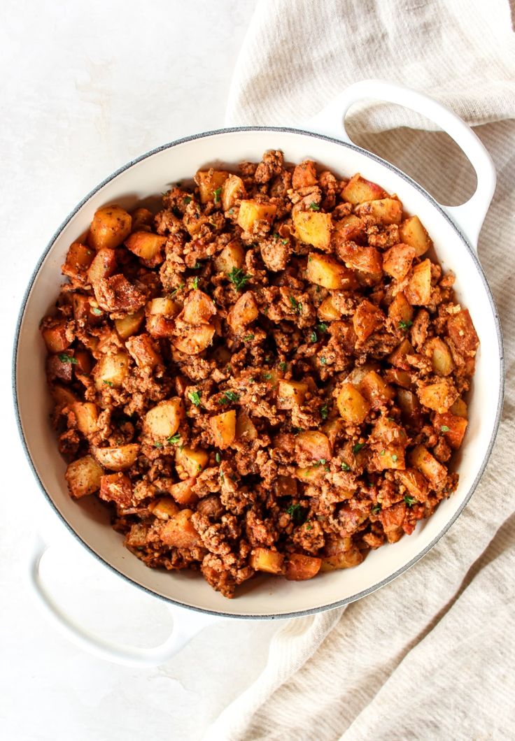 a bowl filled with meat and potatoes on top of a white table cloth next to a spoon