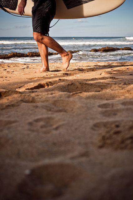 a man carrying a surfboard on top of a sandy beach