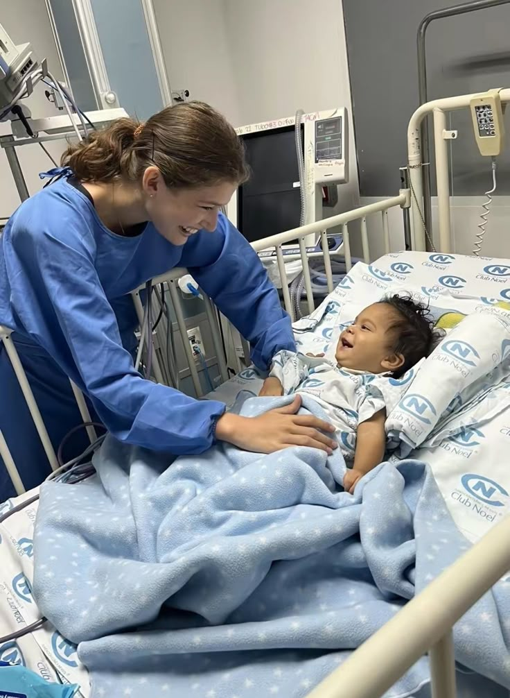 a woman in blue scrubs tending to a baby in a hospital bed with an iv