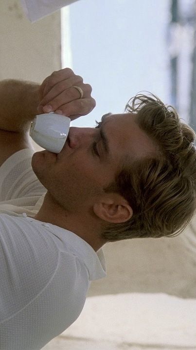 a man in white shirt using an electric hair dryer on his head while leaning against a wall