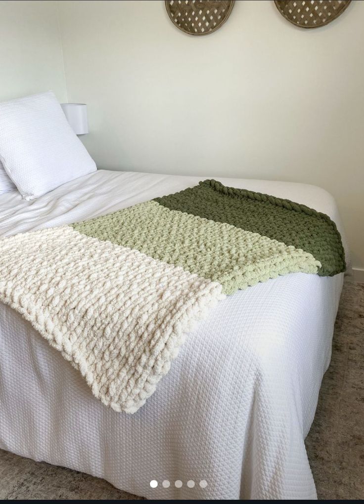 a white bed topped with a green and white blanket next to two pictures on the wall