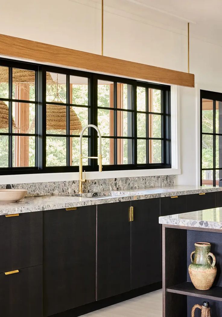 a kitchen with black cabinets and marble counter tops, an island in the middle is surrounded by open windows