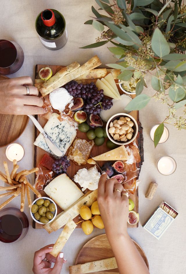 two hands reaching for cheese and olives on a platter