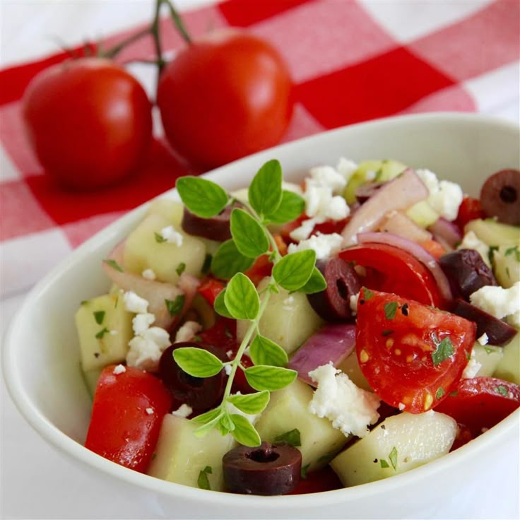 a salad with tomatoes, olives and feta cheese in a white bowl on a checkered tablecloth