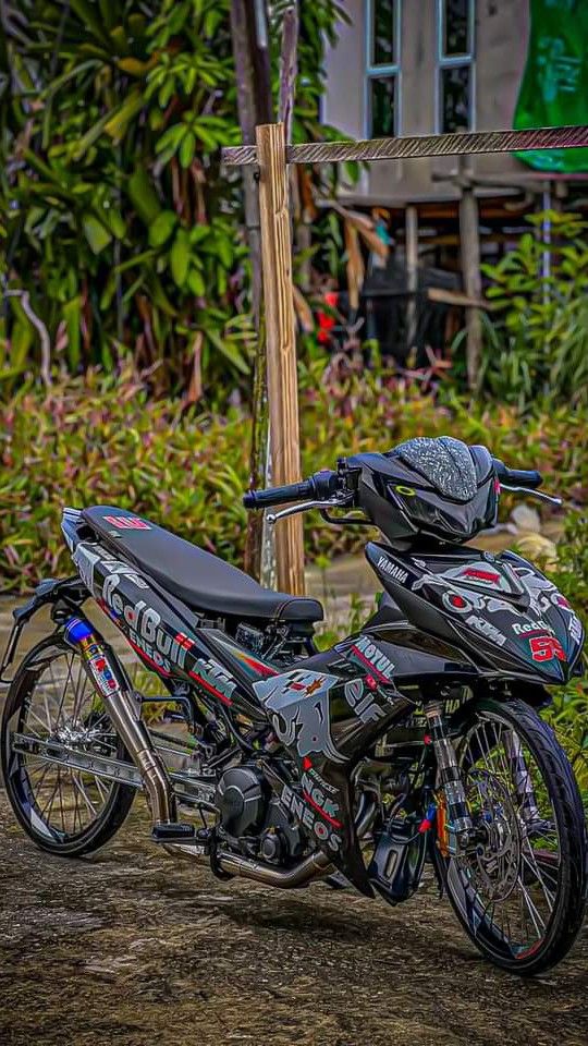 a motorcycle parked on the side of a dirt road next to bushes and trees in front of a building