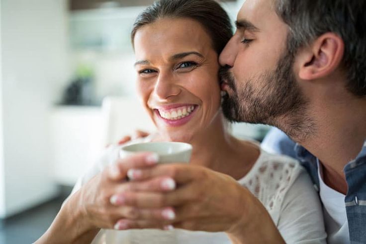 a man kissing a woman while holding a cup in her hand and smiling at the camera