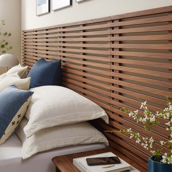 a bed with white pillows and wooden slatted headboard next to a window