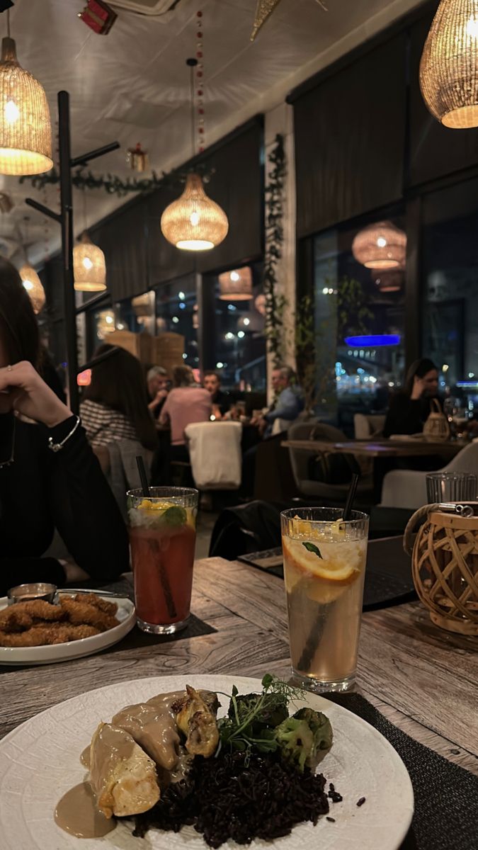 a woman sitting at a table with food in front of her and drinks on the side