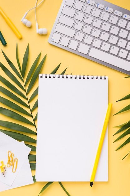 an overhead view of a notepad, keyboard and various office supplies on a yellow background