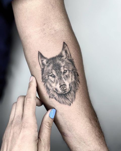 a black and white photo of a wolf tattoo on the left arm with blue eyes