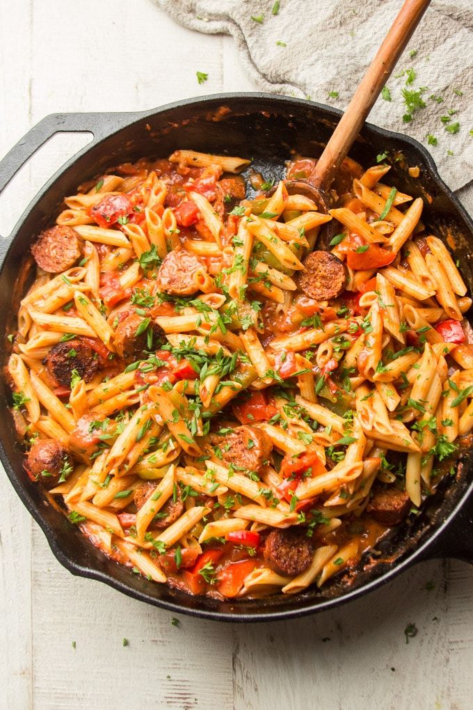 a skillet filled with pasta, sausage and tomato sauce on top of a wooden table